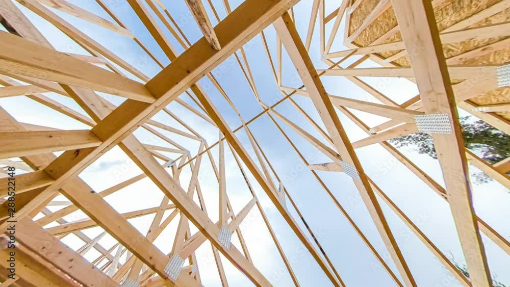 4k time lapse clip of wood roof beams of a new home construction site under blue sky and clouds passing by