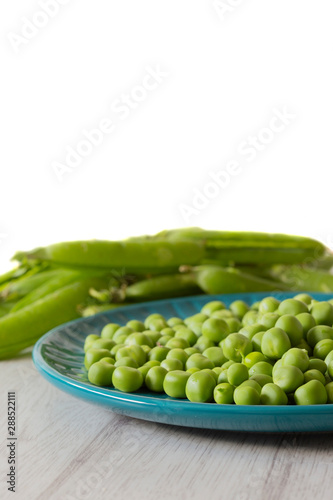 Garden peas with pods on a blue plate.  Grey wood background