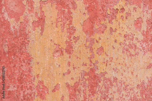 Old weathered painted wall background texture. Red dirty peeled plaster wall with falling off flakes of paint.