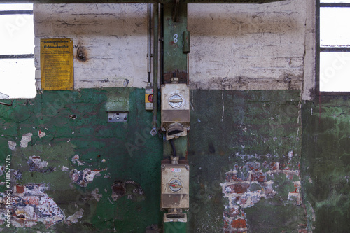 Front view of electric meter, Circuit Breaker and Electric wires system on rough old scratch painted with white and green brick wall in abandon industrial building. © Peeradontax