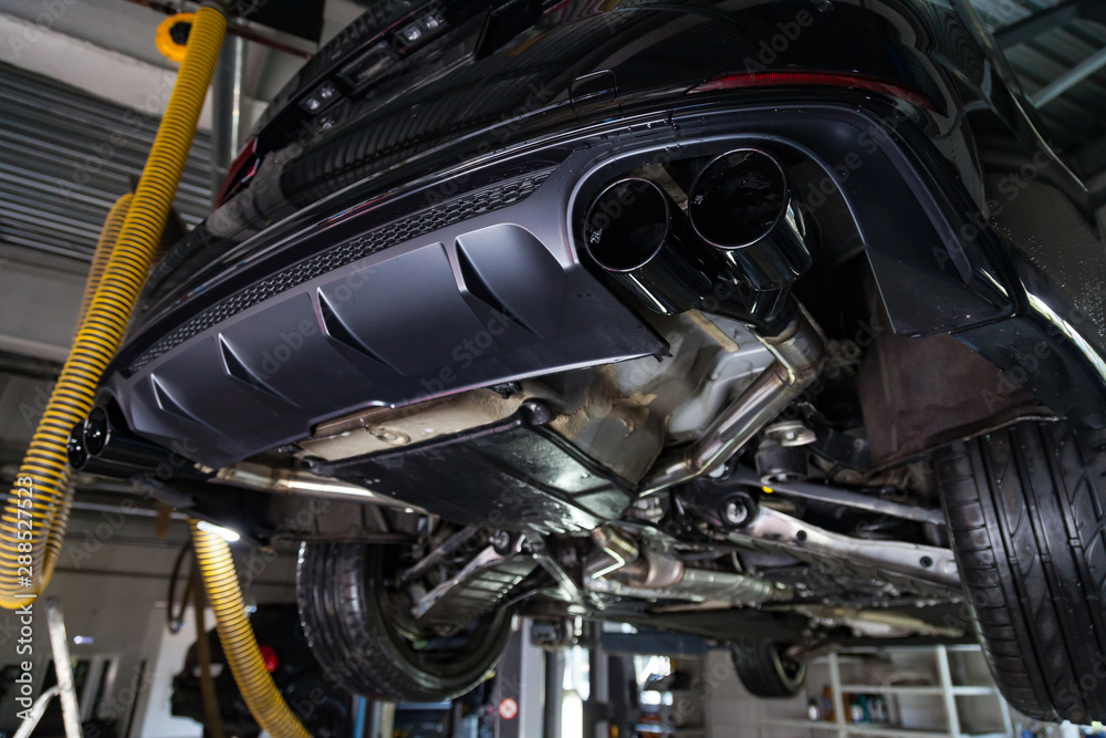 Bottom view of the car on a bifurcated exhaust system, rear bumper with a sports diffuser and nozzles in black. Tuning and atom service industry. Bottom view of the car on a bifurcated exhaust system, rear bumper with a sports diffuser and nozzles in black. Tuning and atom service industry.