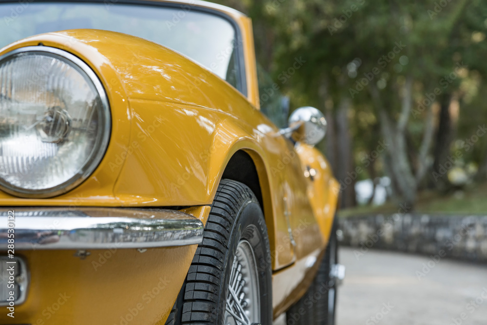 A fragment of a vintage convertible yellow. In the foreground-the left side of the car, in the background-the Park area. Selective focus.