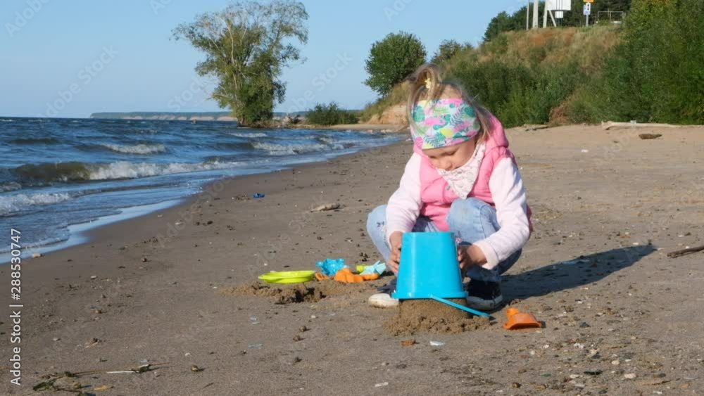 Cute little girl playing along sandy beach in slow motion. Little girl walking along beach. Little girl slowly walking alone at seashore. Child going for a walk on sea waves on beach Cute little girl playing along sandy beach in slow motion. Little girl walking along beach. Little girl slowly walking alone at seashore. Child going for a walk on sea waves on beach