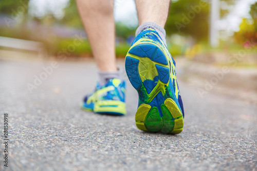 Close up on shoe, Runner athlete feet running on road under sunlight in the morning.
