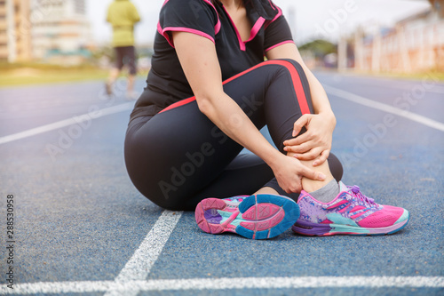 Female runner athlete ankle injury and pain. Woman suffering from painful ankle while running on the blue rubberized running track. © Oranuch