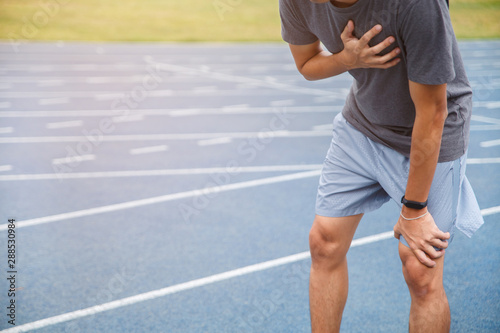 Man runner athlete chest injury and pain. Man suffering from painful chest or Symptoms of heart disease while running on the blue rubberized running track.