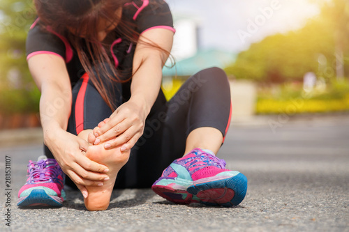 Female runner athlete foot injury and pain. Woman suffering from painful foot while running on the road.