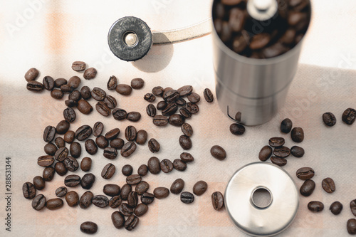 Scattered coffee beans on the kitchen tablecloth background and coffee bean grinder, Natural light, Selcetive focus, Vintage style. photo