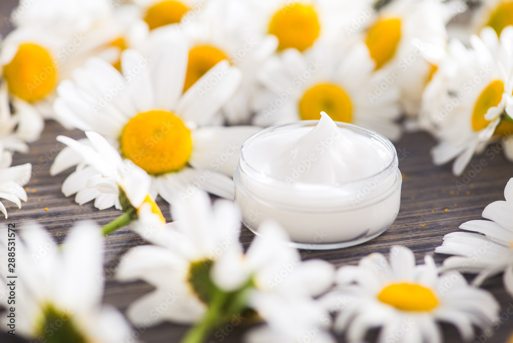 Container with chamomile cream and flowers on a table Container with chamomile cream and flowers on a table