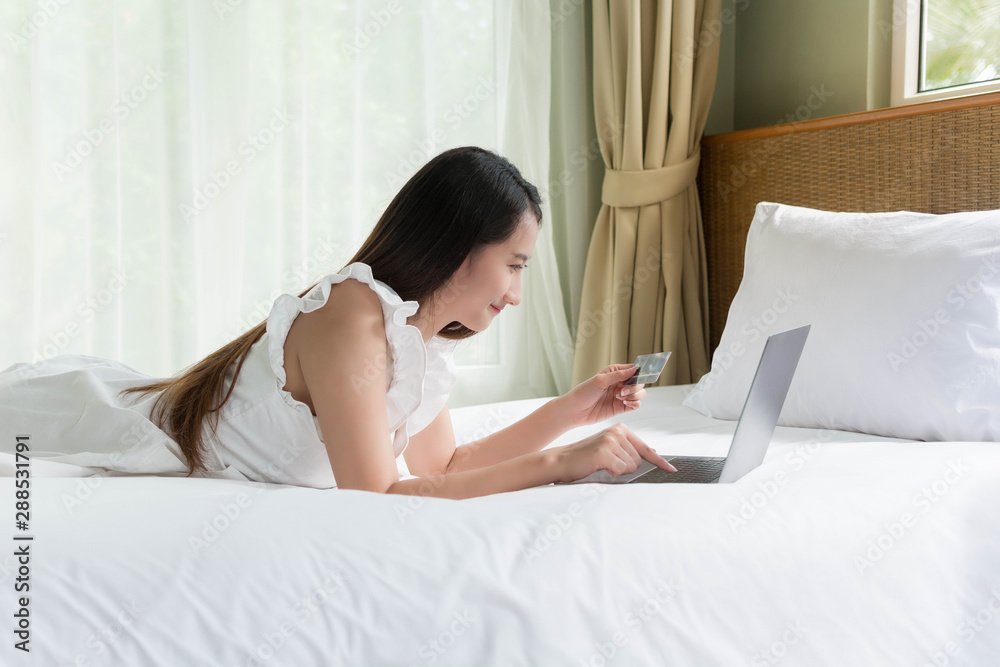 Asia woman holding credit card and using laptop computer inputting card information while shopping online on the bed, Online shopping concept. Asia woman holding credit card and using laptop computer inputting card information while shopping online on the bed, Online shopping concept.