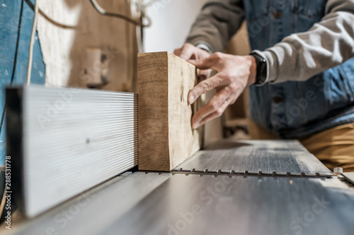 Caucasian man making wooden parts for custom furniture on machine tool called thickness planer in carpentry. Producing lumber concept