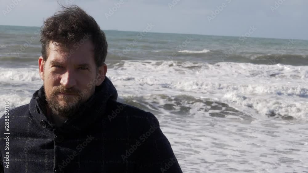Serious man looking camera standing in front of waves of ocean slow motion Serious man looking camera standing in front of waves of ocean slow motion