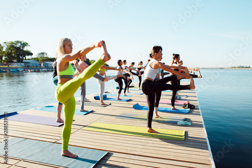 A big group of people attending yoga classes on a pontoon near the lake.