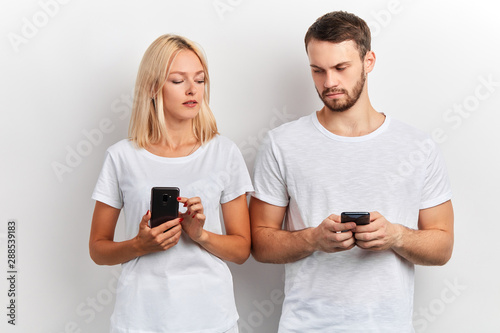Billede på lærred two attractive people comparing their smart phones, close up portrait, isolated