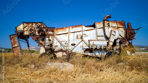 Eine verrostete Erntemaschine auf einem Getreidefelder vor blauem Himmel