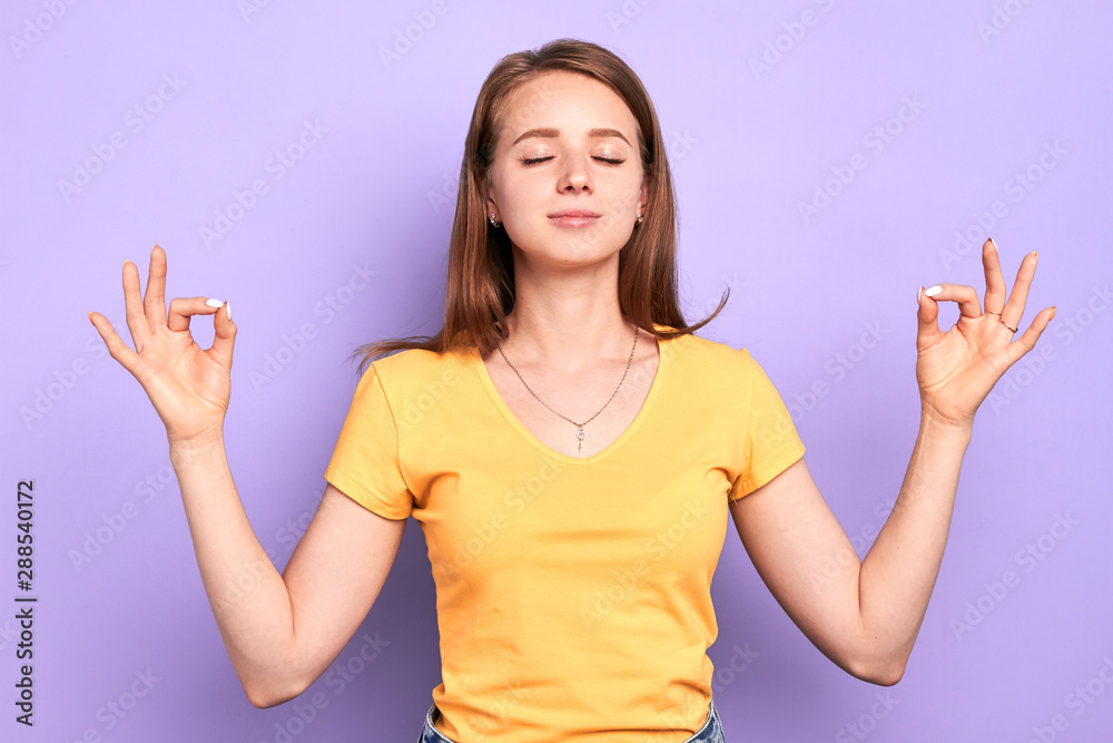 Front view of young beautiful female yoga instructor with peaceful face expression, doing breath exercises, meditates indoors with closed eyes, tries to relax and calm down. Front view of young beautiful female yoga instructor with peaceful face expression, doing breath exercises, meditates indoors with closed eyes, tries to relax and calm down.