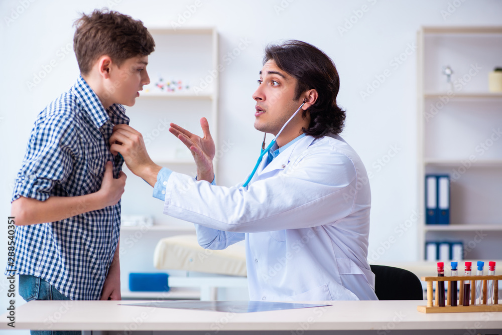 Fototapeta premium Male doctor examining boy by stethoscope