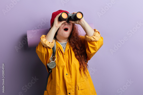 astonished surprised young ginger woman looking through the binoculars at the distance, close up photo. copy space photo