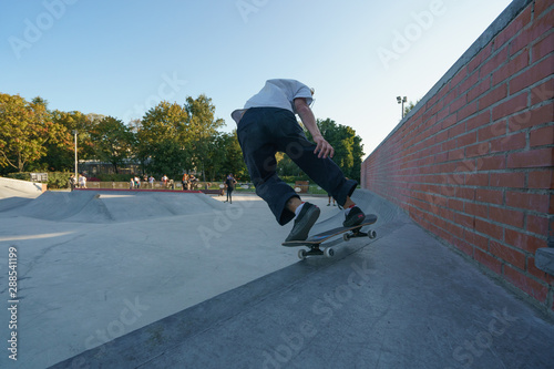 Skateboarder performs trick on city sports ground in summer day. He has tough unsafe practice. He glides on a sloping wall. Extreme sport is very popular among youth.