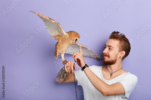 Obraz na plátně young man teaching an owl to obey the commands, tasks, actions