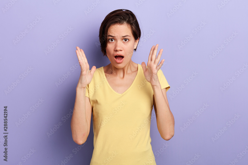 Surprised young emotional woman with short black hair shouting, expresseing shock, keeps palms near face over violet background.isolated blue background Surprised young emotional woman with short black hair shouting, expresseing shock, keeps palms near face over violet background.isolated blue background