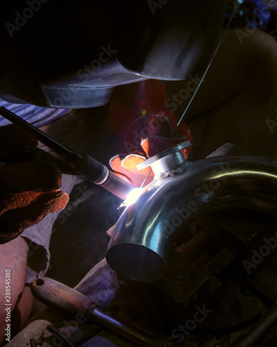 man works argon welding repairs aluminum pipe in the garage of the house