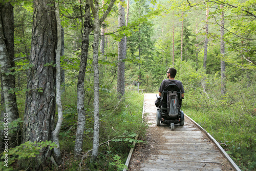 Happy man on wheelchair in nature. Exploring forest wilderness on an accessible dirt path.