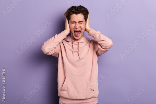 Young crazy funny emotional man covering his ears and shouting.young man screaming, he doesn't want to listen to his wife. conflict, problem guy ignoring his girlfriend . close up portrait