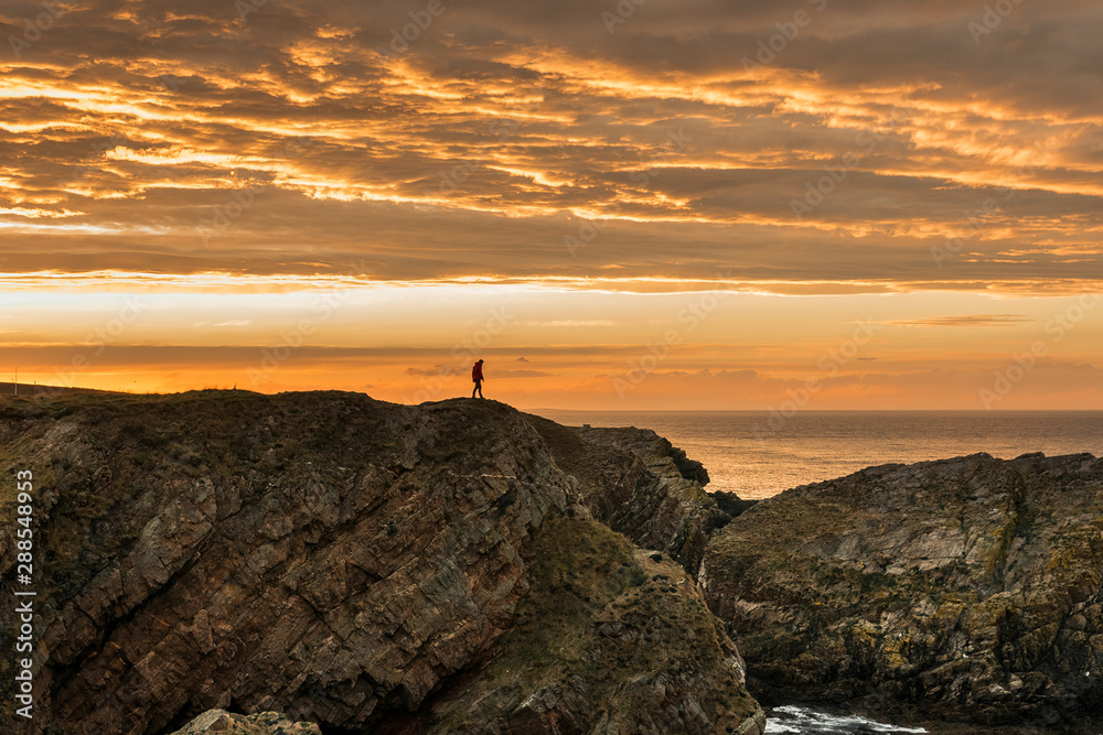 Fototapeta premium Person in shadow walking in a cliff on a sunset with an impresive orange sky