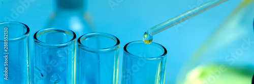 Pipette tip with a droplet over a rack of Eppendorf test tubes. Close up. Blue toning.