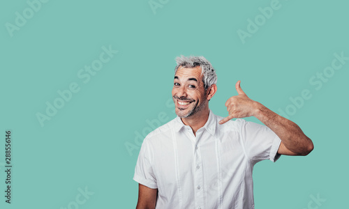 Human facial expressions concept. Call me back please! Young attractive guy in casual t shirt, makes phone sign, wants to speak with someone via cell phone. Body language concept. photo