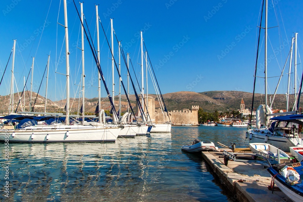 Obraz premium Summer morning in the harbor. Yachts parking in harbor, Harbor in Trogir, Croatia. Sailboats reflected in water. Boat rental.