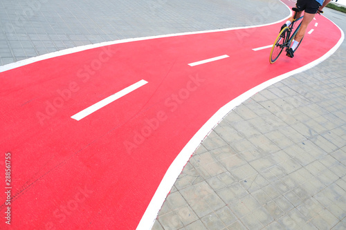 A red biking path in the city with a male figure of a biker moving away in perspective view.