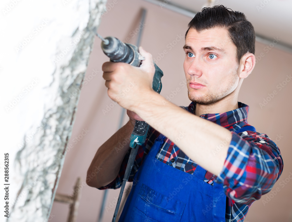 Naklejka premium attentive builder drilling hole in wall with perforator