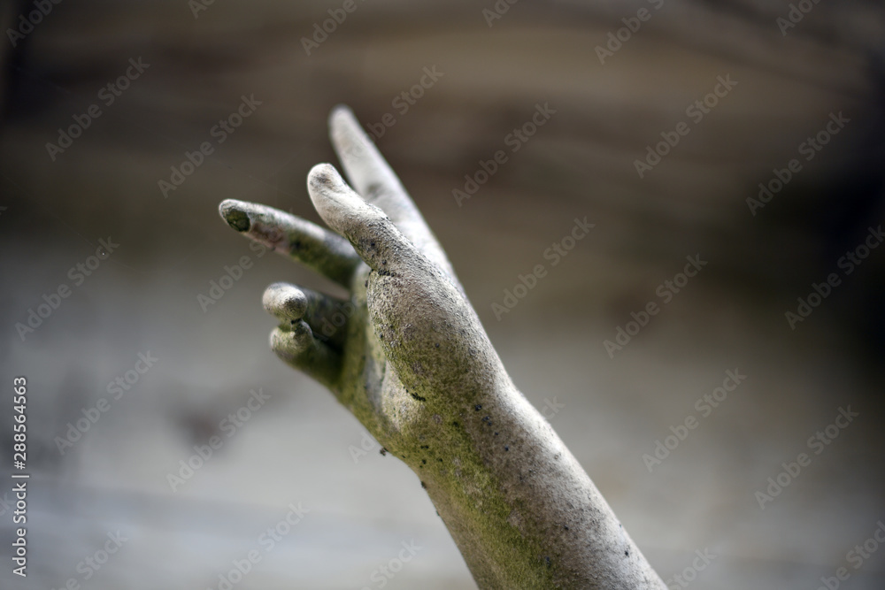 A hand rises in the air. The hand of an old sandstone sculpture.