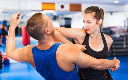 Kobieta trenuje z mężczyzną na kursie samoobrony w siłowni.
