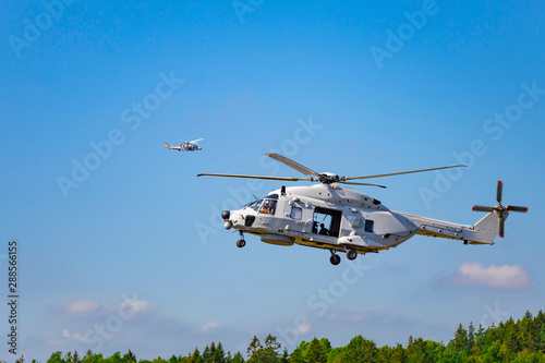 Landing of swedish military helicopter. Swedish Air Force in action near forest under blue sky with clouds