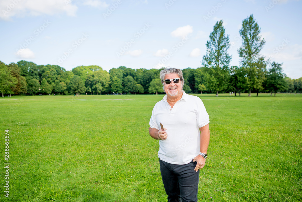 Man poses with a smartphone in a public green park during a summer day