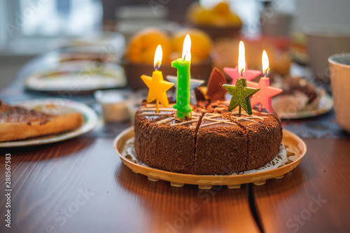 Chocolate birthday cake surrounded by lit candles for a first birthday or anniversary celebration on a table, happy birthday for child, close up phoography