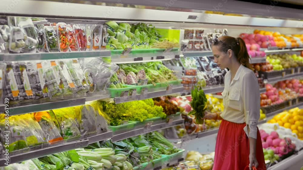 Young american woman choose and smell green salad standing in supermarket. Beautiful female buying vegan bio product, having time in organic shop. Portrait of 30s lady customer making purchase during Young american woman choose and smell green salad standing in supermarket. Beautiful female buying vegan bio product, having time in organic shop. Portrait of 30s lady customer making purchase during