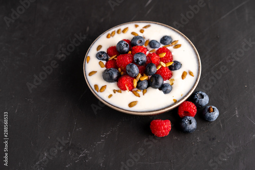 Tasty fresh blueberry raspberries  yoghurt shake dessert in ceramic bowl standing on black dark table background.