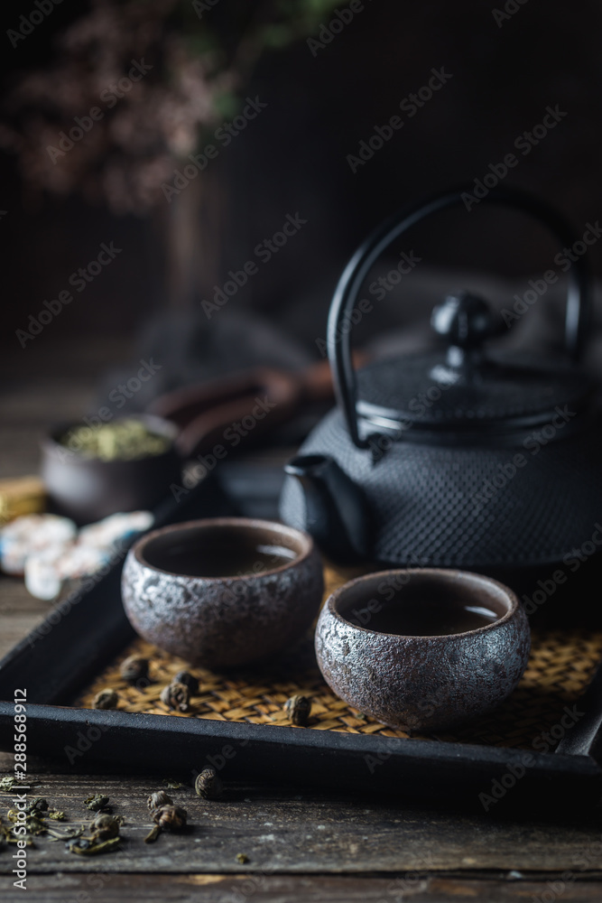 Still-life of japanese healthy green tea in a small cups and teapot over dark background