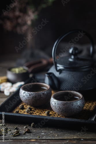 Still-life of japanese healthy green tea in a small cups and teapot over dark background