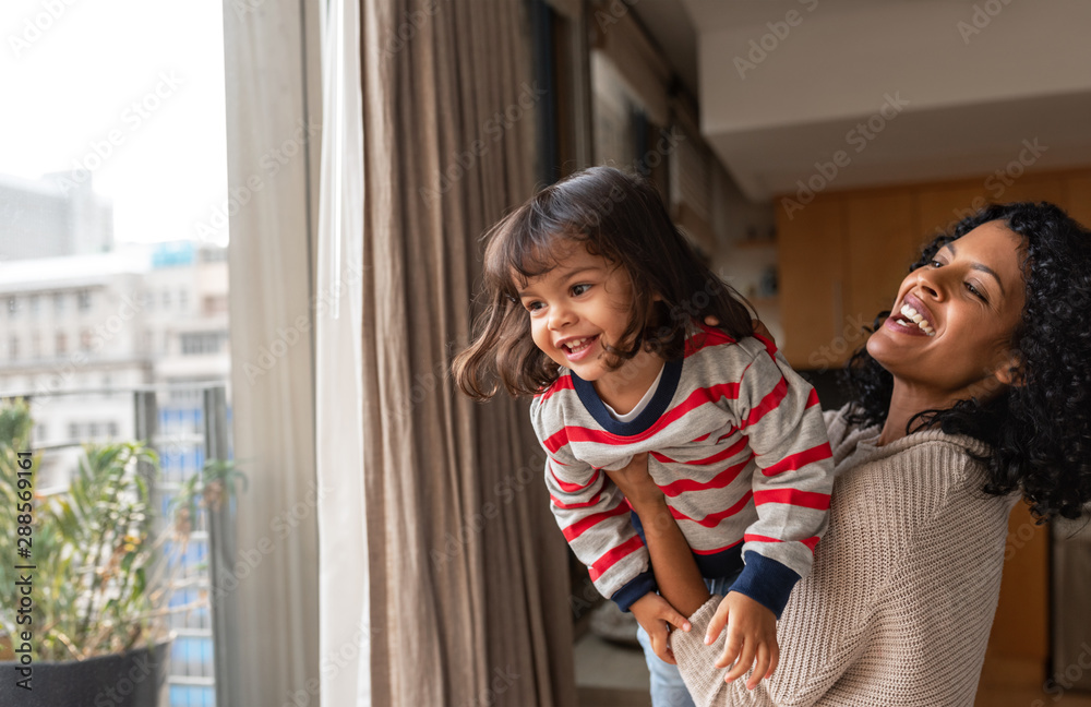Laughing mother and small daughter playing together at home - obrazy, fototapety, plakaty 