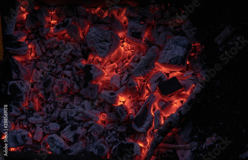The texture of the coal fire. Actively smoldering embers of fire. Background of burning hot coals. Flicker of burning coals at night