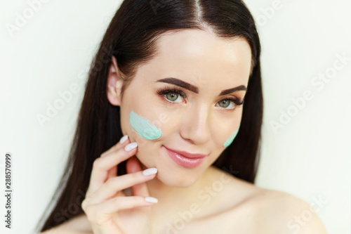 Portrait of brunette woman with healthy glow perfect smooth skin. Model with long eyelashes and beautiful green eyes. Young girl enjoys gray clay facial mask. 