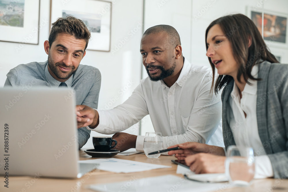 Obraz premium Smiling businesspeople working with a laptop during an office meeting