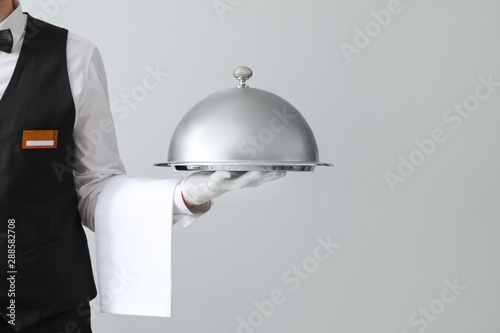Handsome waiter with tray and cloche on light background photo