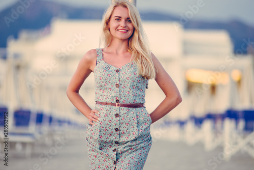 Blonde caucasian woman with an elegant fashionable dress and her wooden bag posing in a portrait session near the sea at sunset