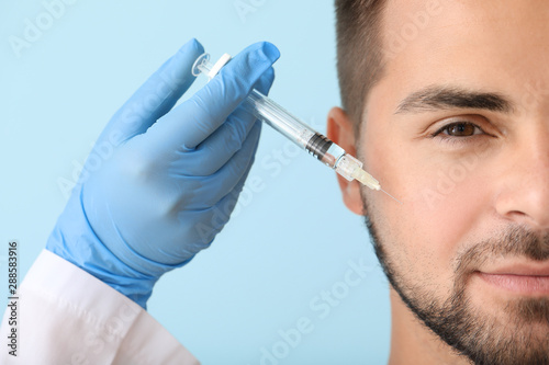 Handsome man receiving filler injection on color background